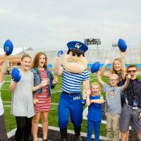 Kids holding up footballs, yelling with Louie and Laker at the Jamie Hosford Football Center dedication.
